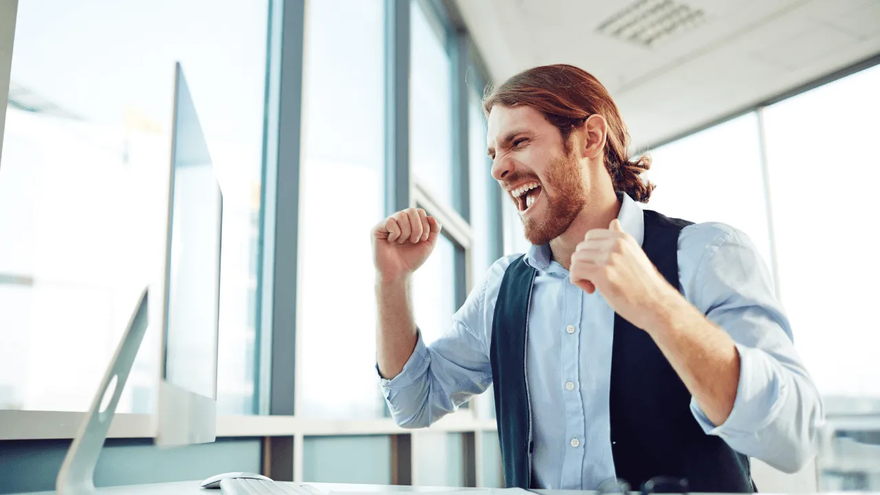 man sitting at his desk celebrating an approval