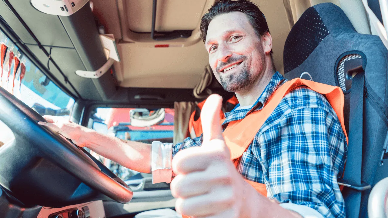 A truck driver sitting in his truck, smiling at the camera while giving a thumbs up