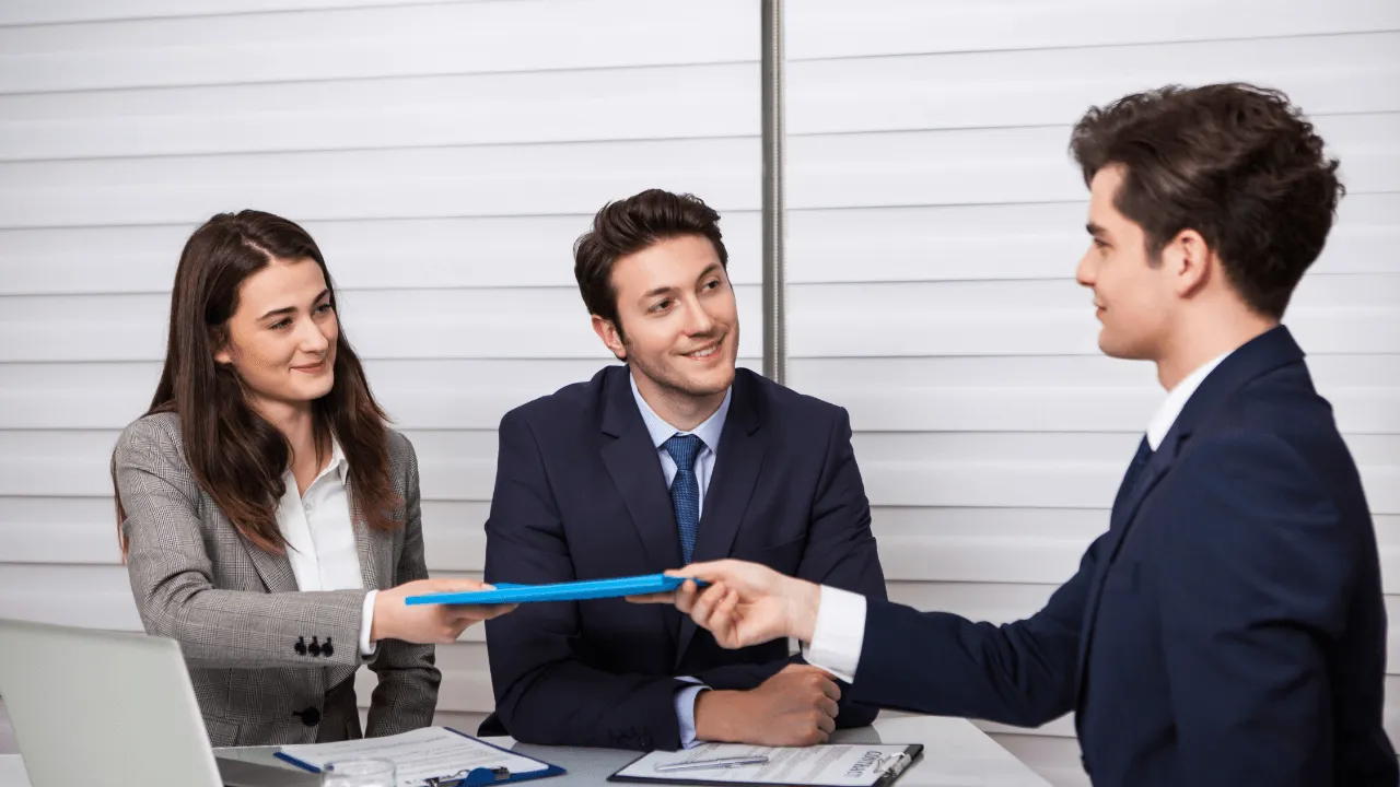 An office team of 3 at a meeting. One team member passes a folder to another