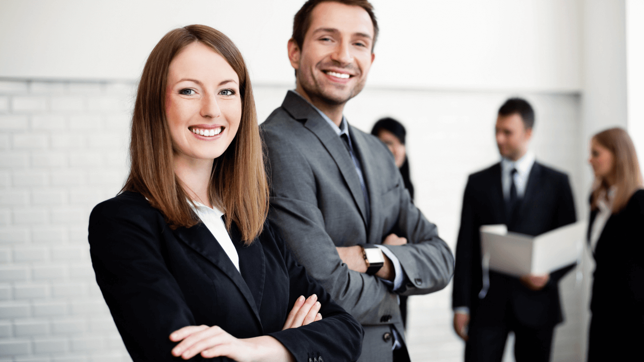 Two business people smiling in an office full of people