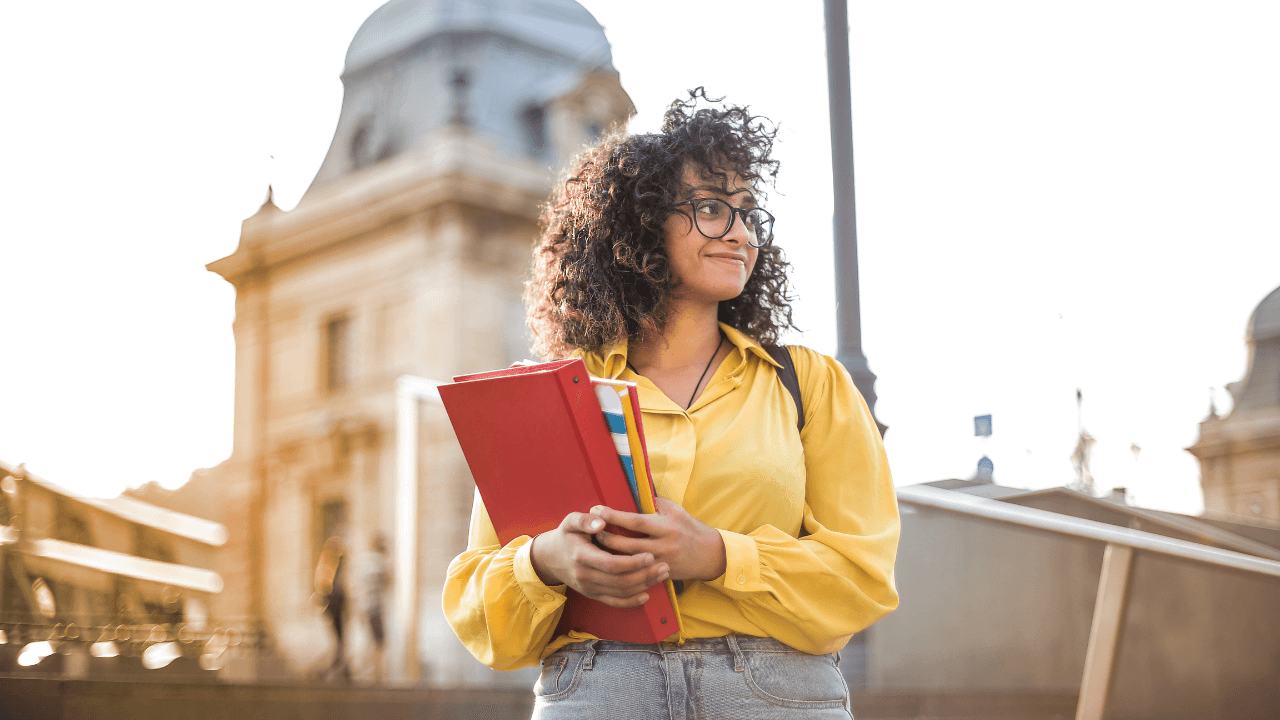 An international student holding her school books while standing outside the school