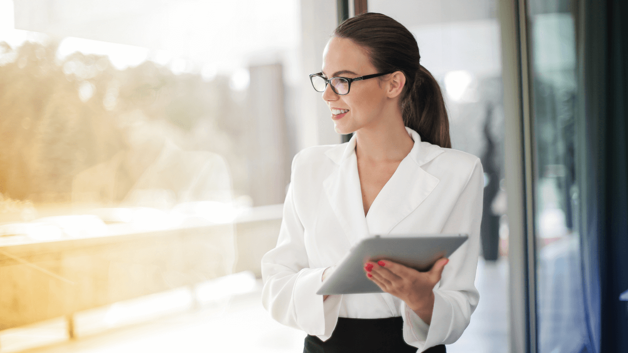 A professional standing in her office holding a tablet while smiling