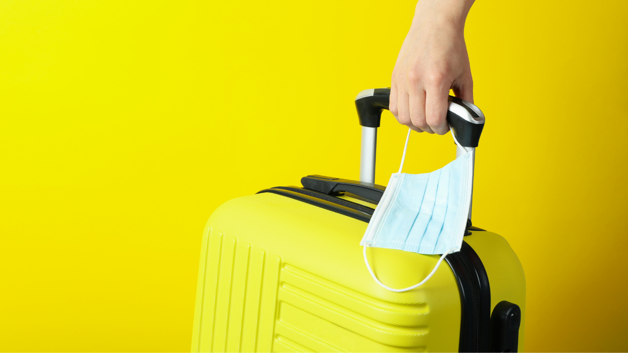 man pulling a yellow suitcase while holding a mask