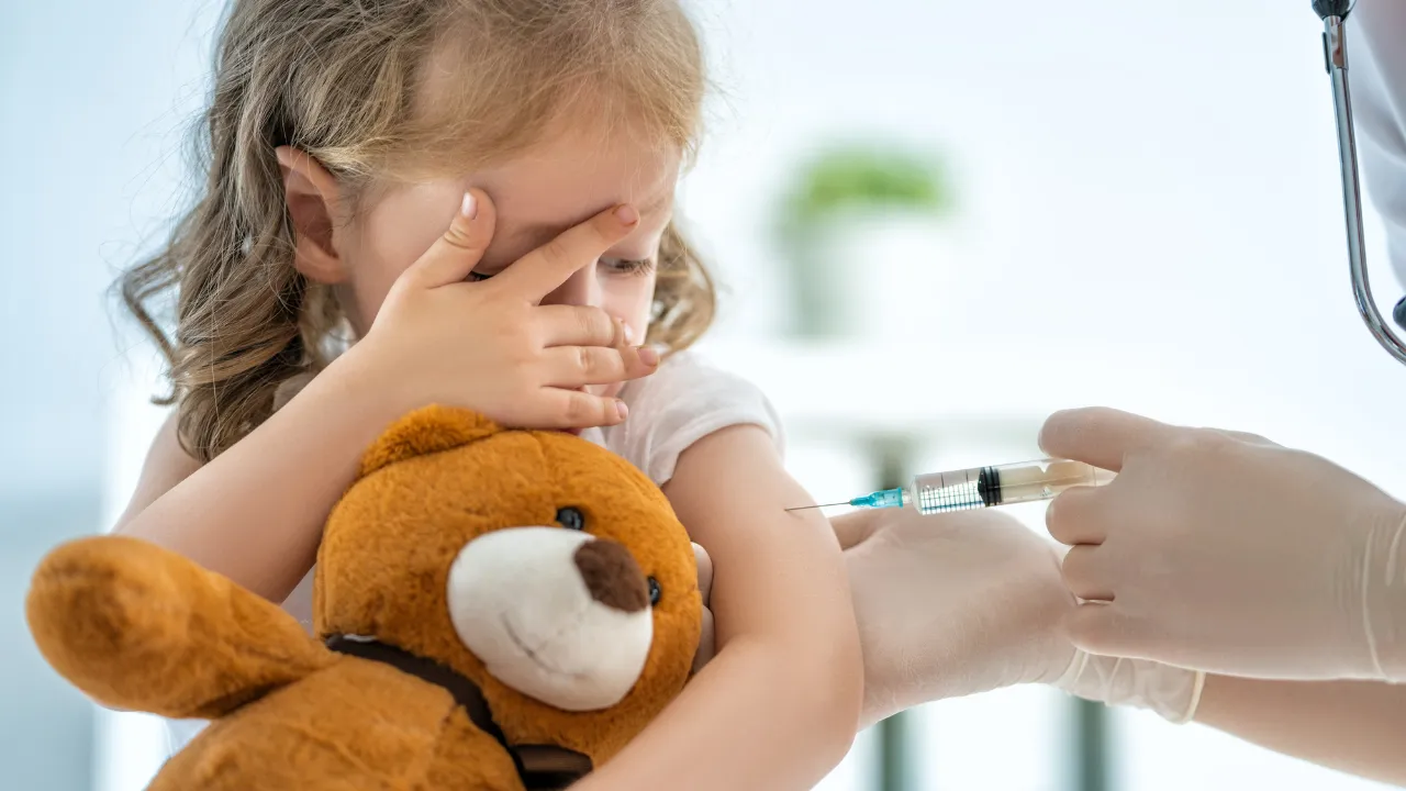 a kid and her teddy bear getting vaccinated