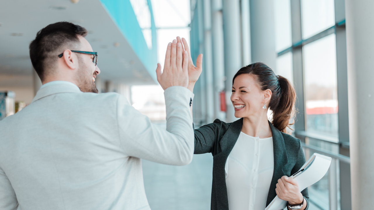 Two employees high fiving each other in the work hallway