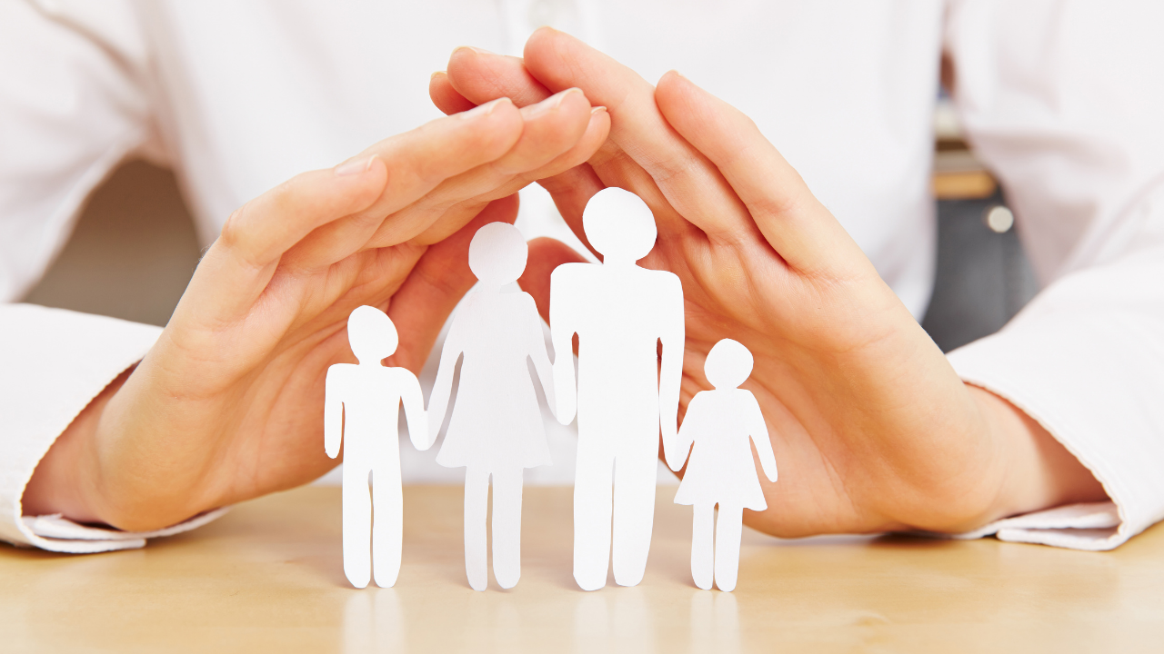 A protecting hand sheltering a paper cut out of a family