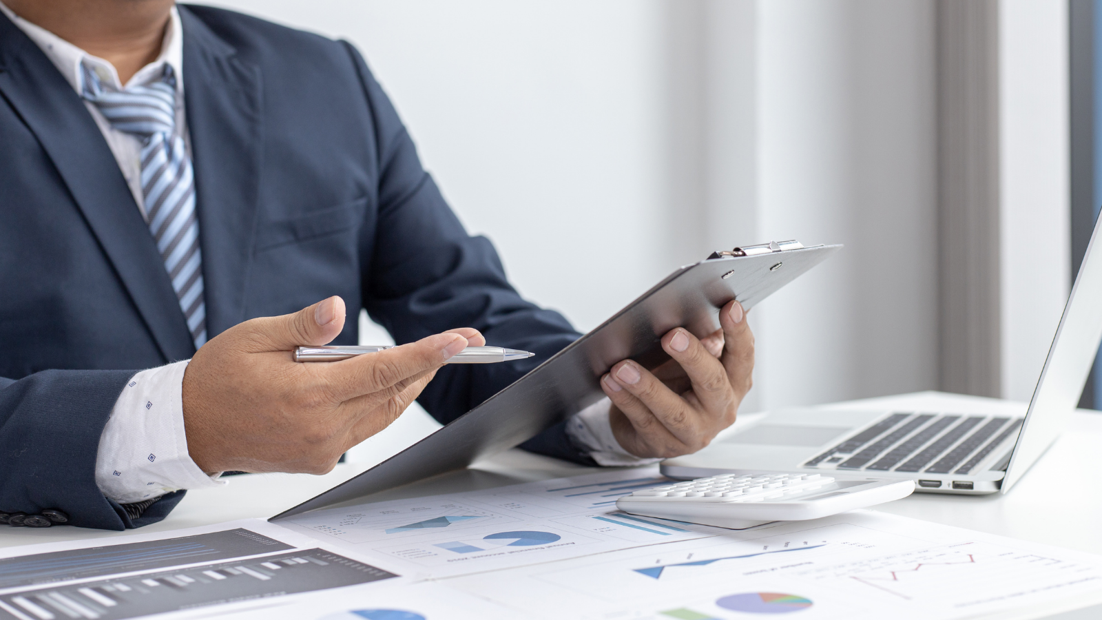 A man working on his laptop while holding a clipboard