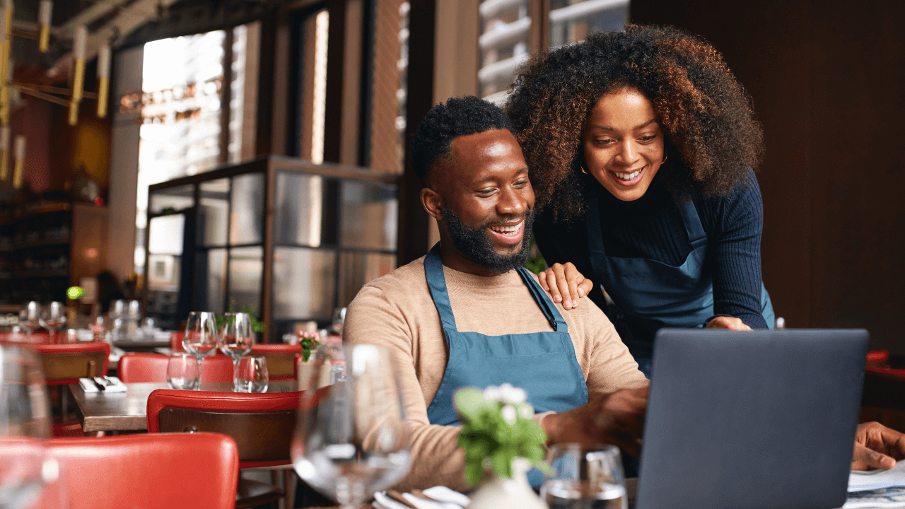 Two business owners smiling at something they are looking at on a laptop