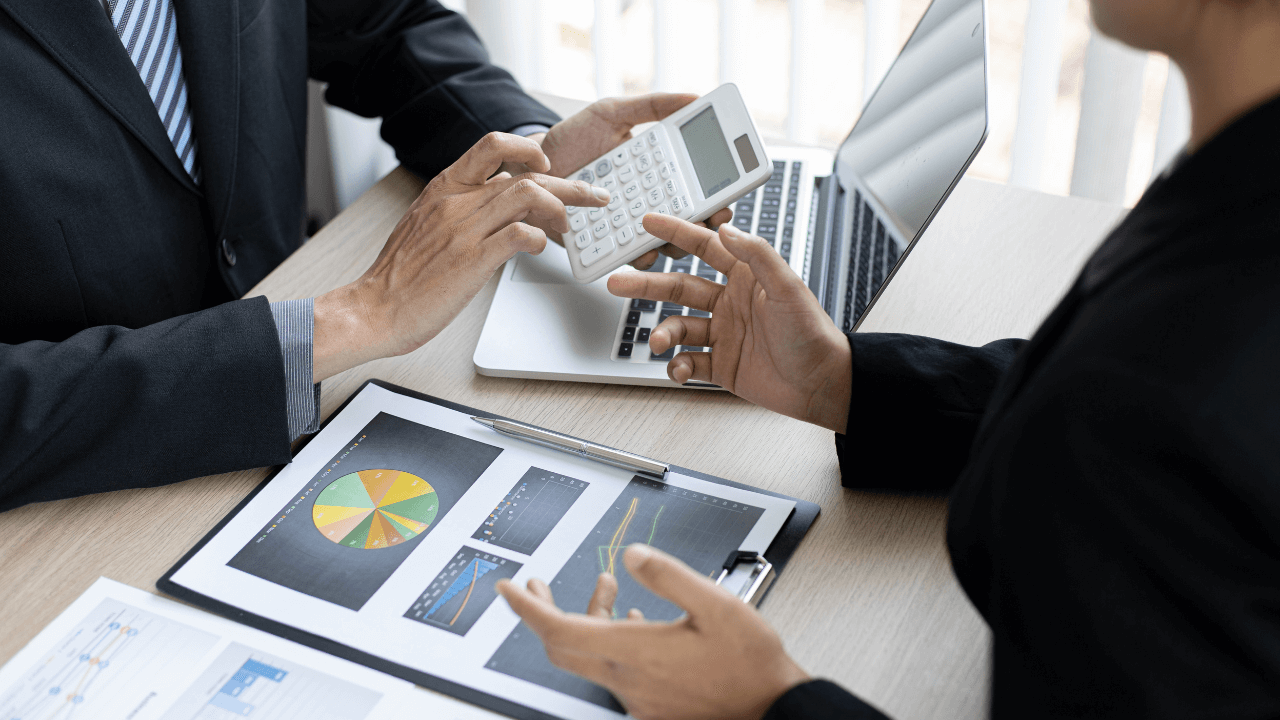 Business associates doing business over a desk of charts while holding a calculator