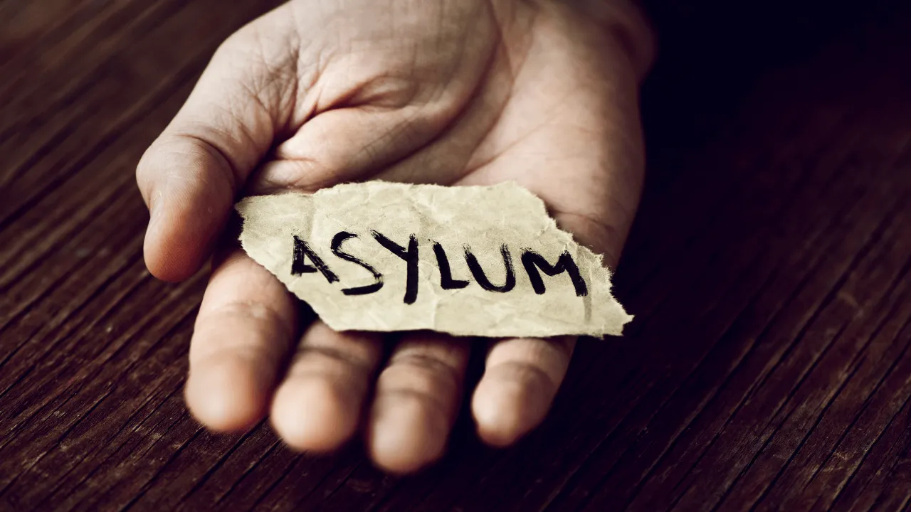 A hand holding a piece of paper that says "asylum" on it