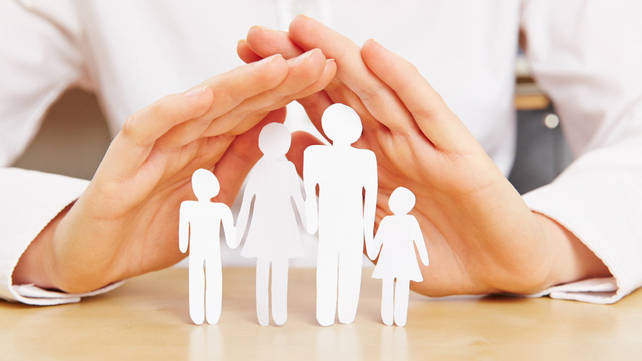 A hand protecting paper cut outs of a family