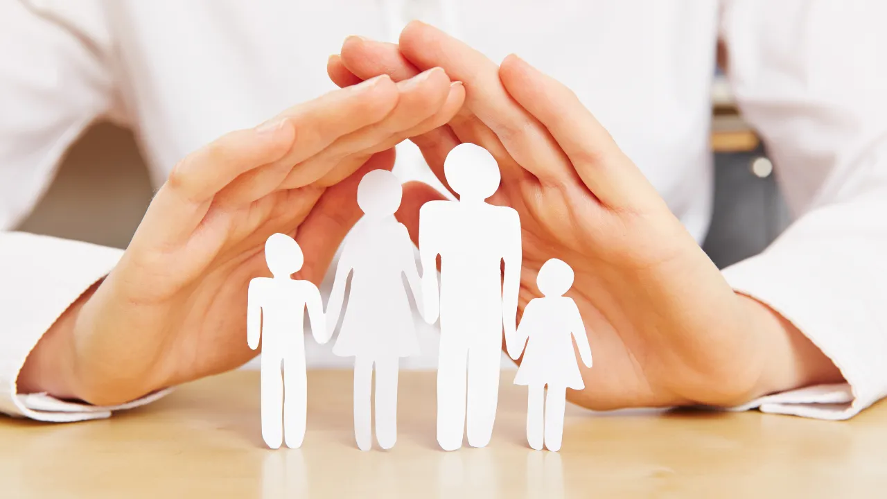 A hand protecting paper cut outs of a family
