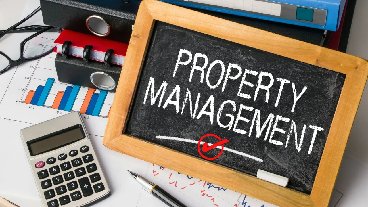 A poroperty management sign on a desk with a calculator, charts, binders, and glasses