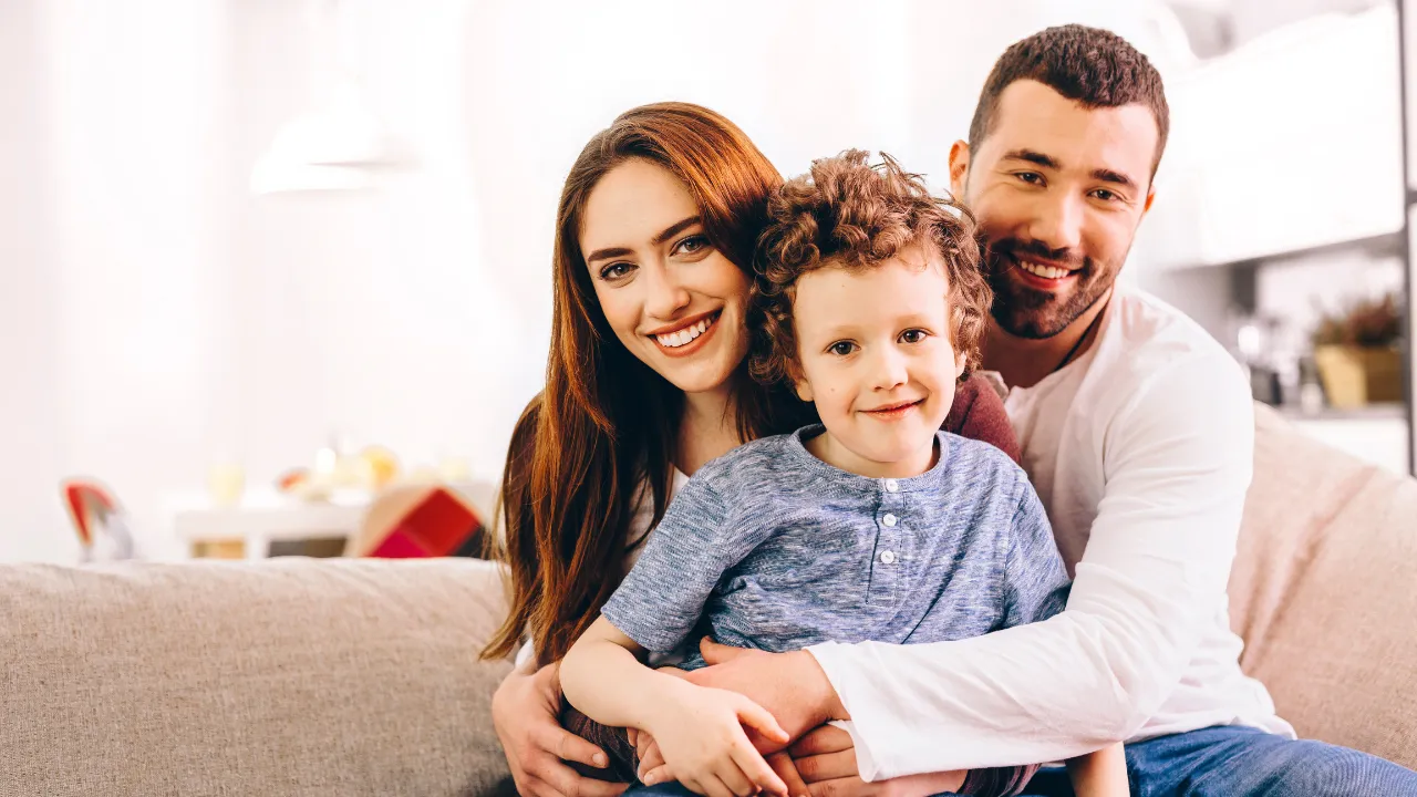 A happy family of 3 sitting on a couch in their home