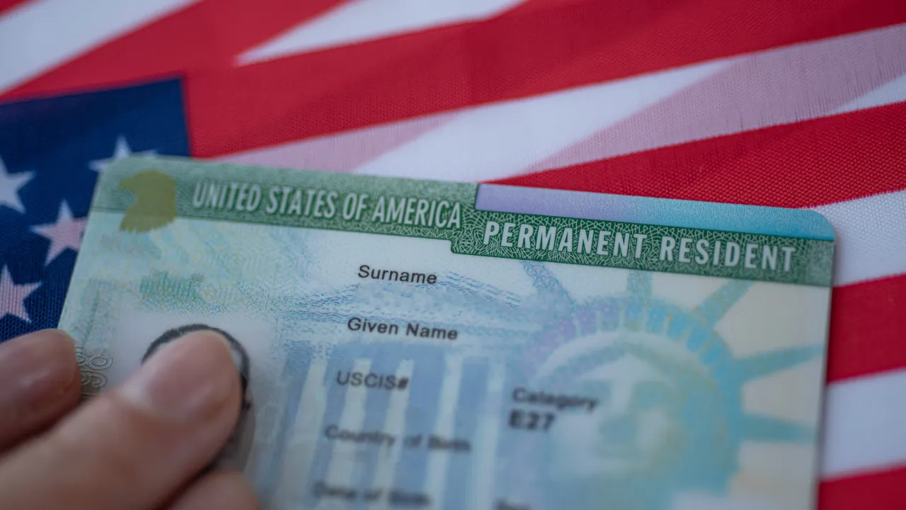 Someone holding a green card by a US flag