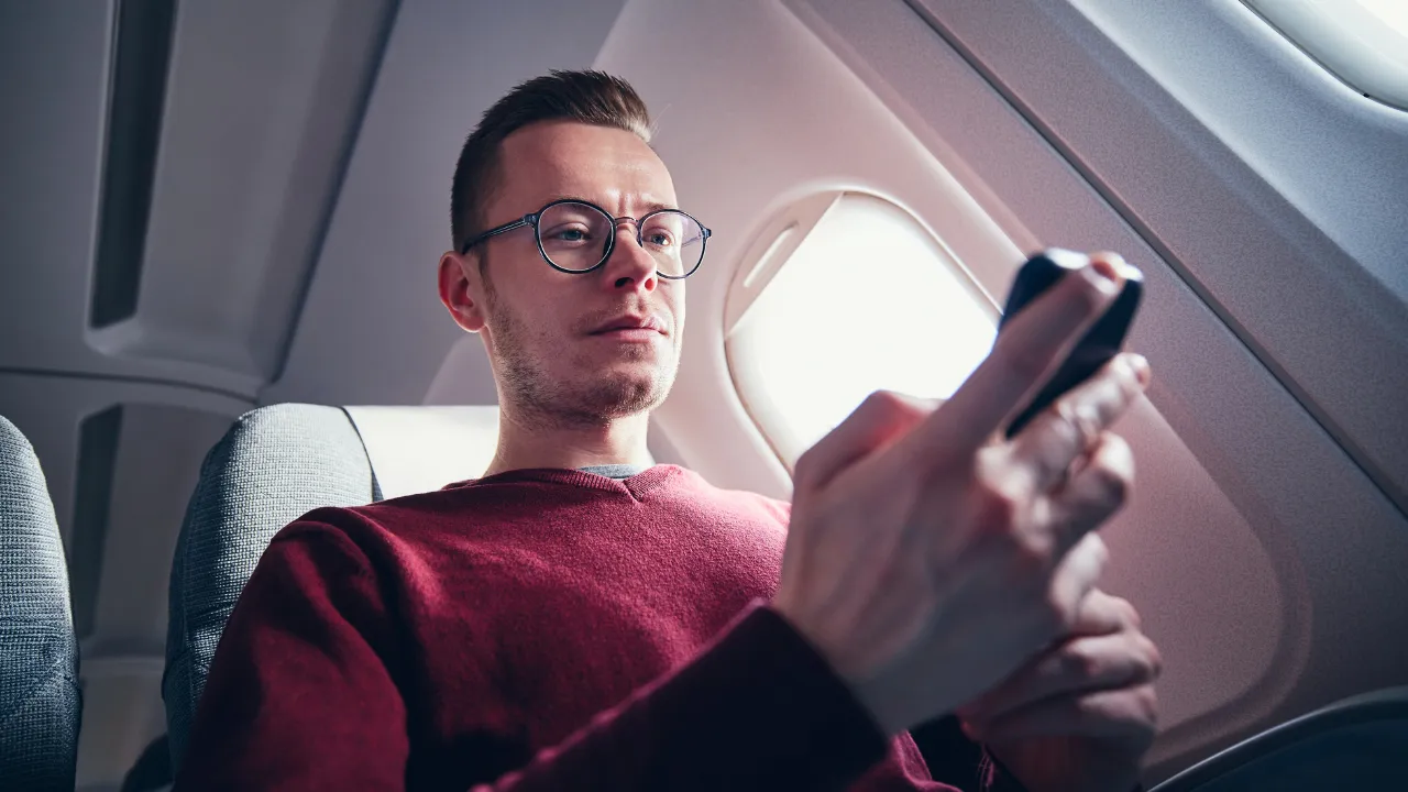 A man checking his connecting flight while on his current flight