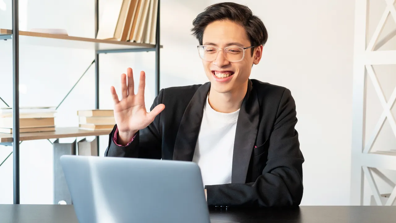 A man smiling at his laptop and waving