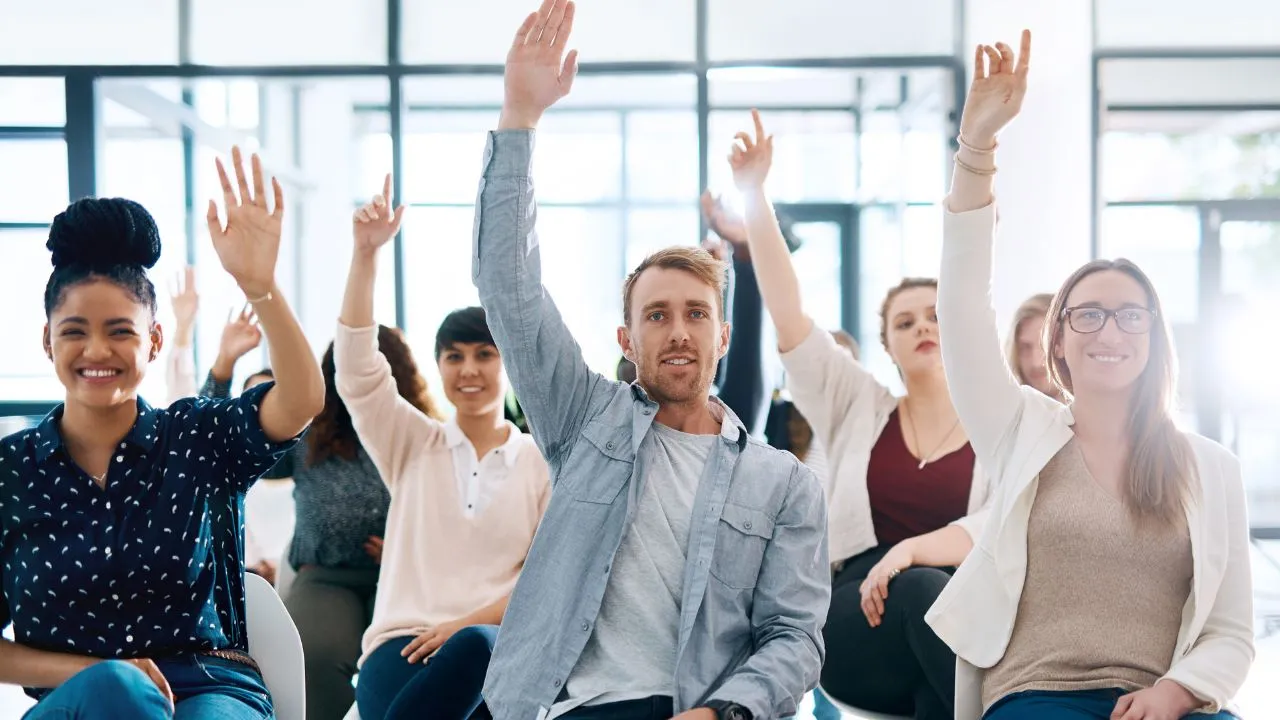 A group of people with their hands raised to ask questions