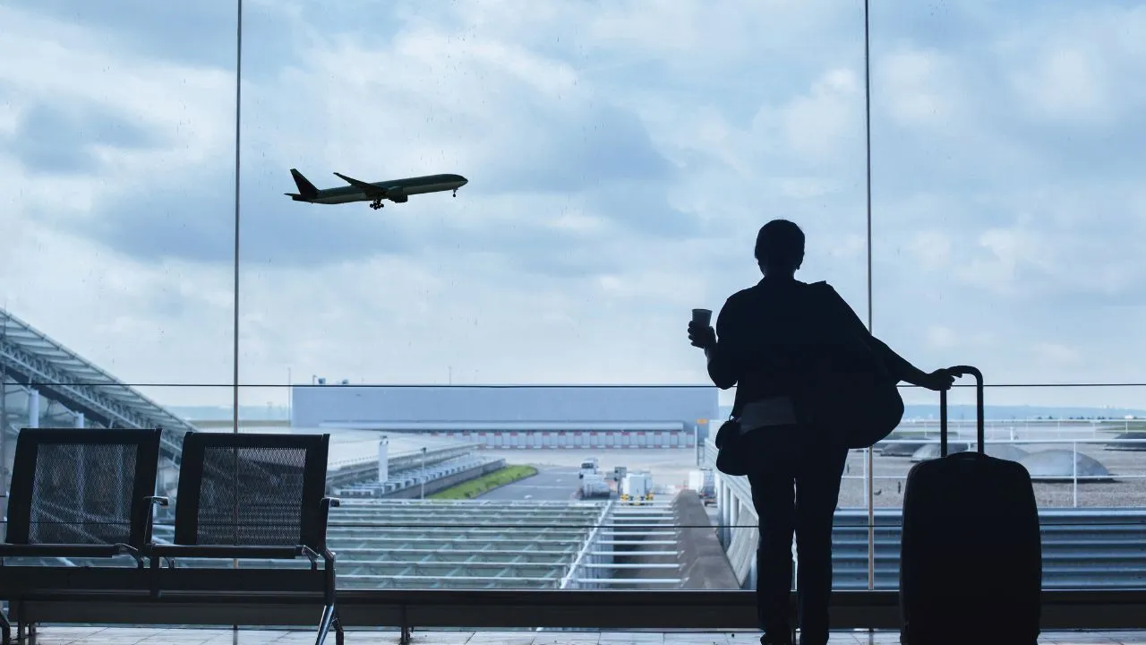 A woman standing in an airport watching planes take off