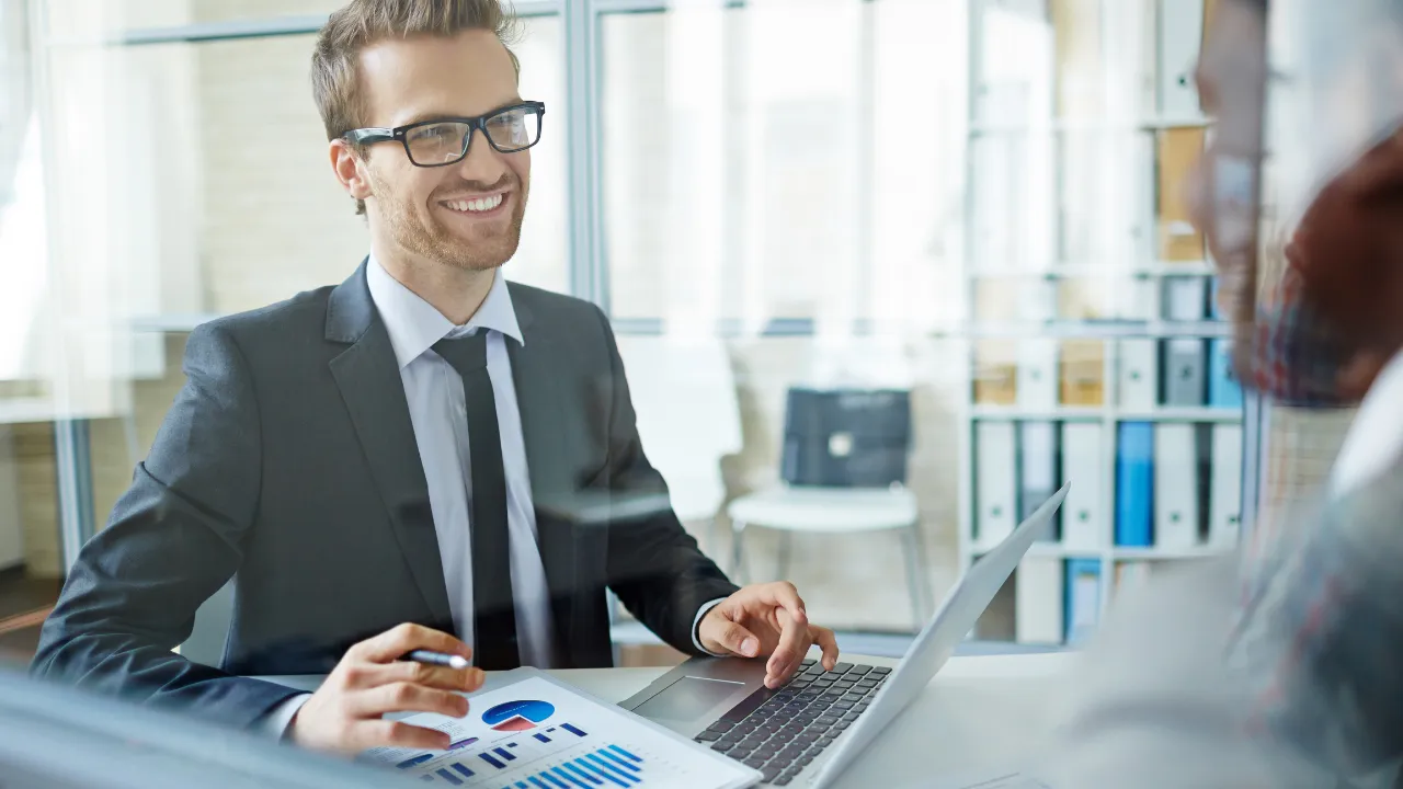 A consultant speaking to a client at his desk with a laptop in front of him