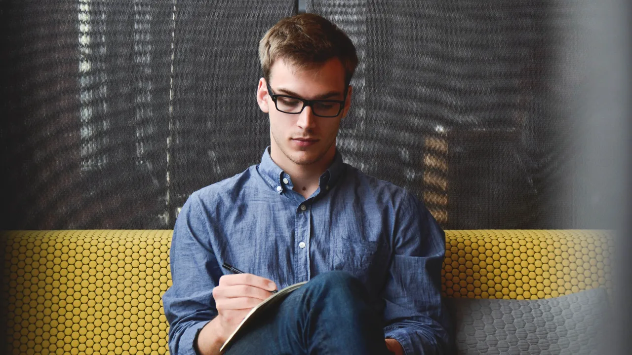 A man writing on pen and paper while sitting down
