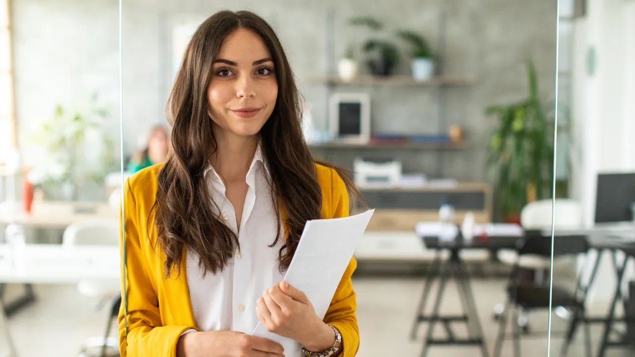 A business professional smiling while holding a stack of papers
