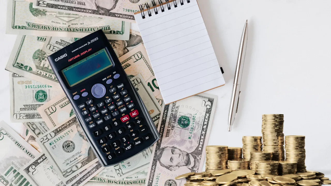 money, a calculator a pen and notepad on a desk
