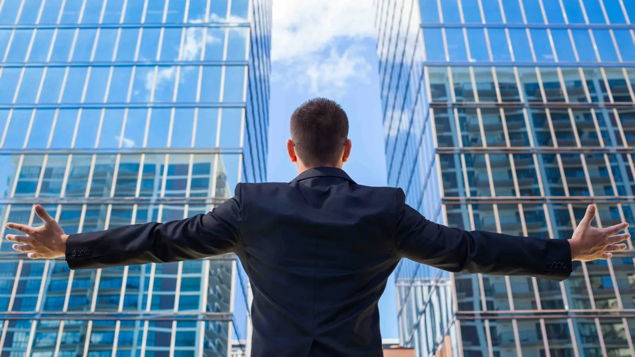 A man standing in front of two large buildings with his arms out stretched