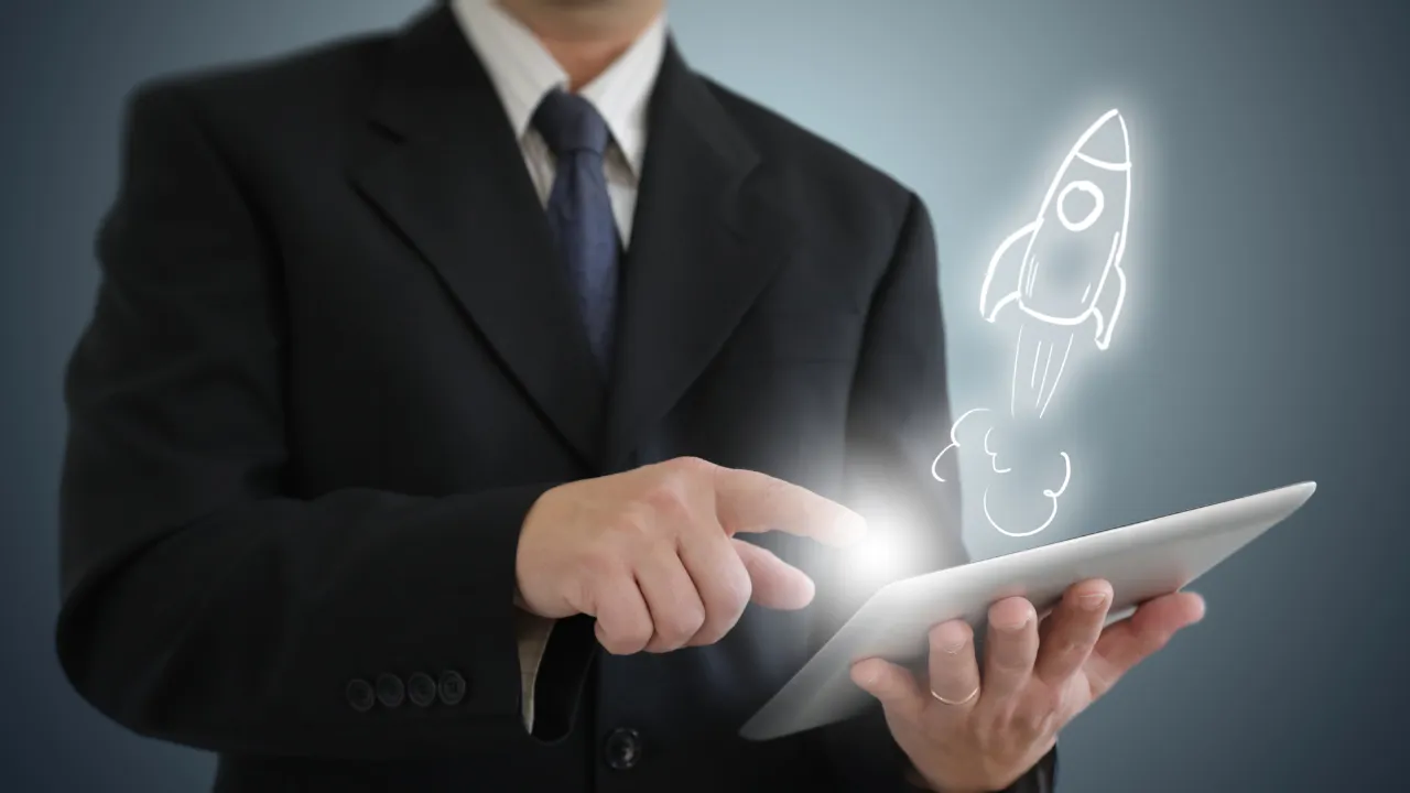 A successful business man holding a tablet with a rocket blasting out of it