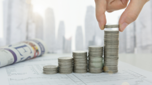 Stacks of coins next to a city backdrop and newspaper.