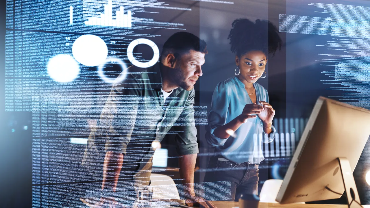 A woman and man looking at a guide and process on a computer