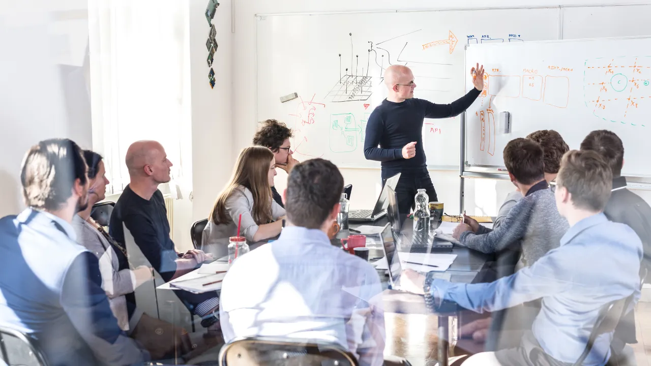 A group of people in a board room around a white board with ideas on it
