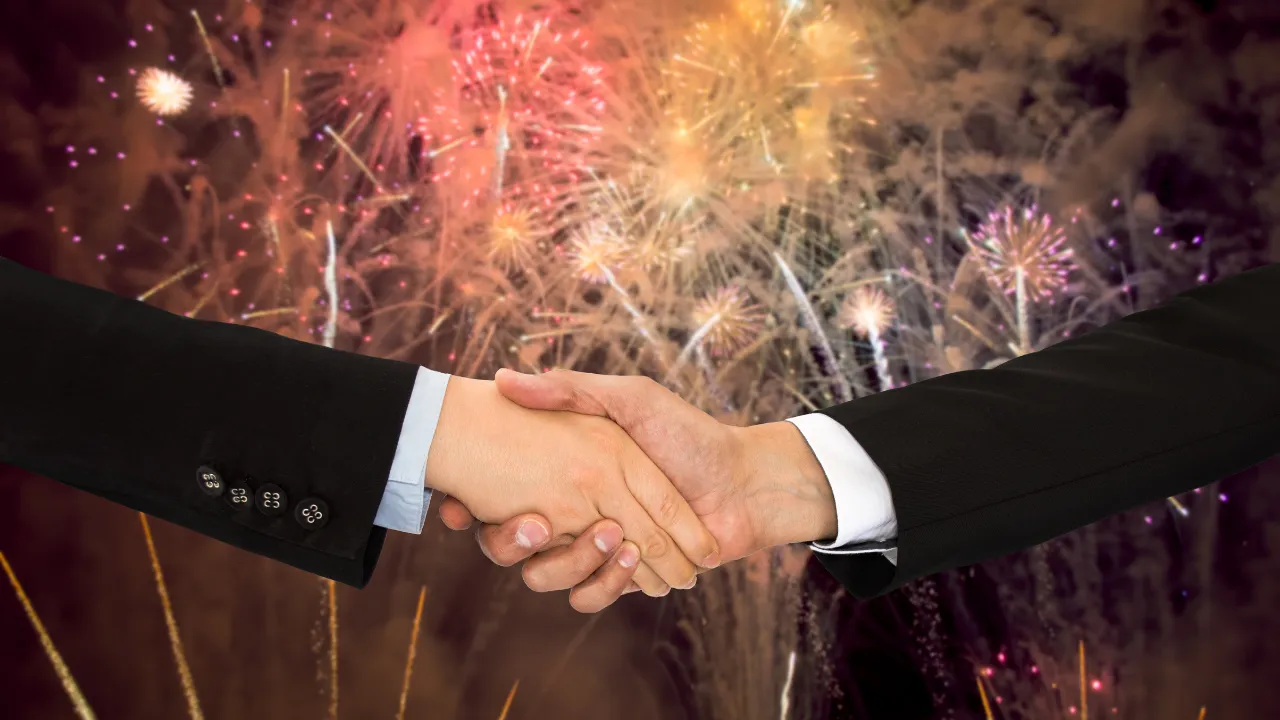 two business professionals shaking hands with fireworks in the background