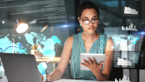 A woman working on a tablet and laptop with global images on the screen