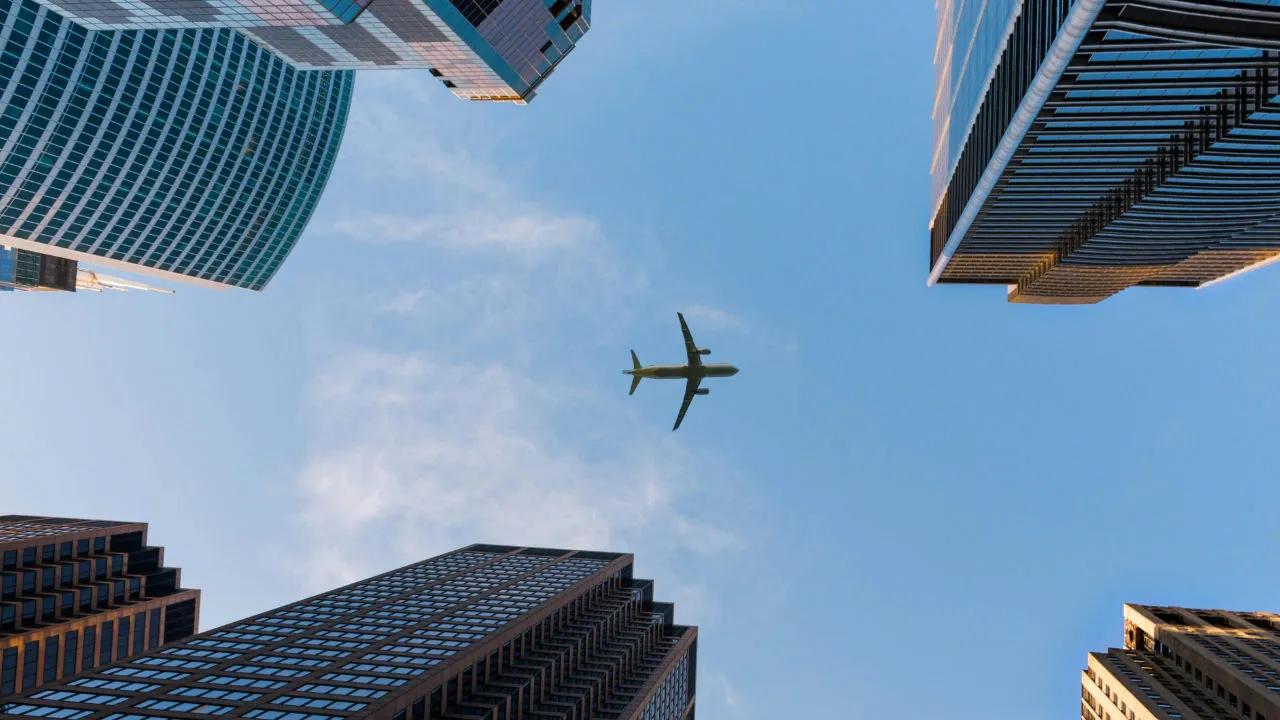 Airplane flying over skyscrapers viewed from below, symbolizing global business and international travel