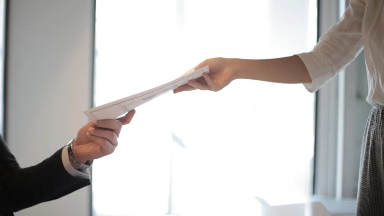 Documents being given from one hand to another between 2 different people.