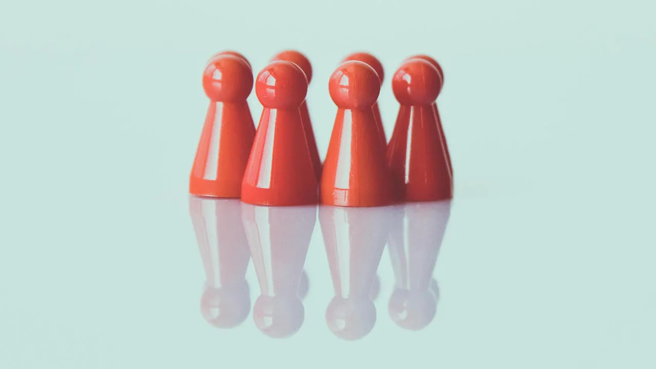 A row of red game pieces standing together on a reflective surface, representing balance and fairness in U.S. visa reciprocity