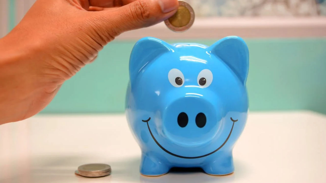 Hand putting coin into blue piggy bank illustrating E-2 visa minimum investment concept