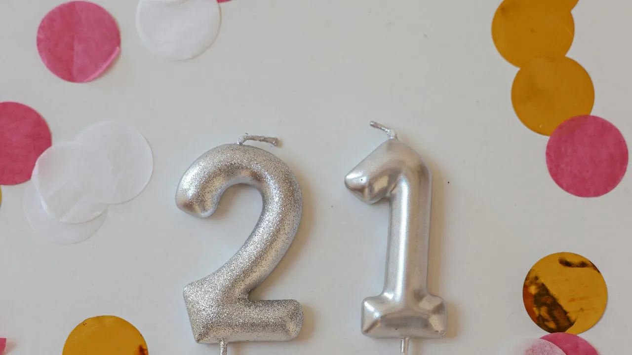 Silver "21" birthday candles surrounded by colorful confetti, representing a child on an E-2 visa turning 21 and needing to find a new visa status.