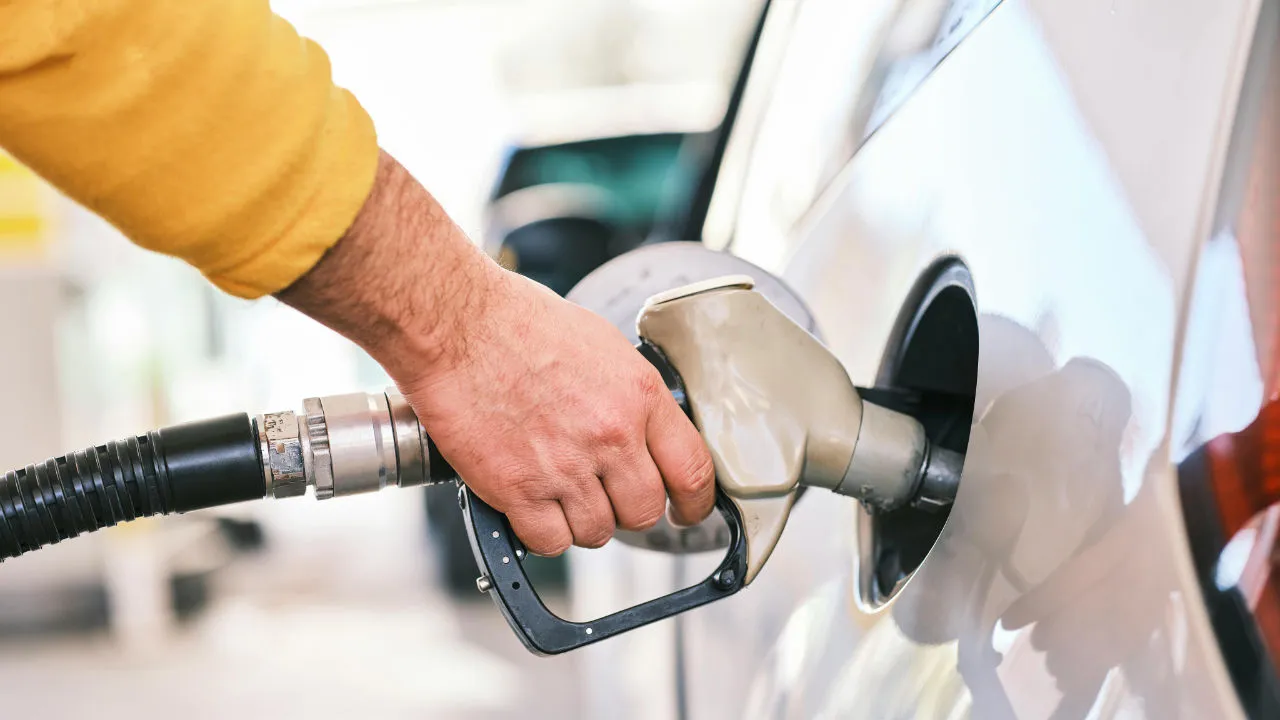 A close-up of a hand holding a gas pump nozzle and inserting it into a silver car's fuel tank.
