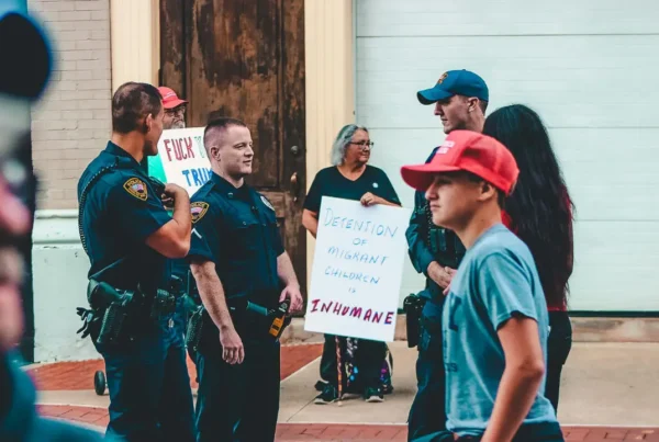 Protesters and police officers at a rally with signs about immigrant detention and deportation.