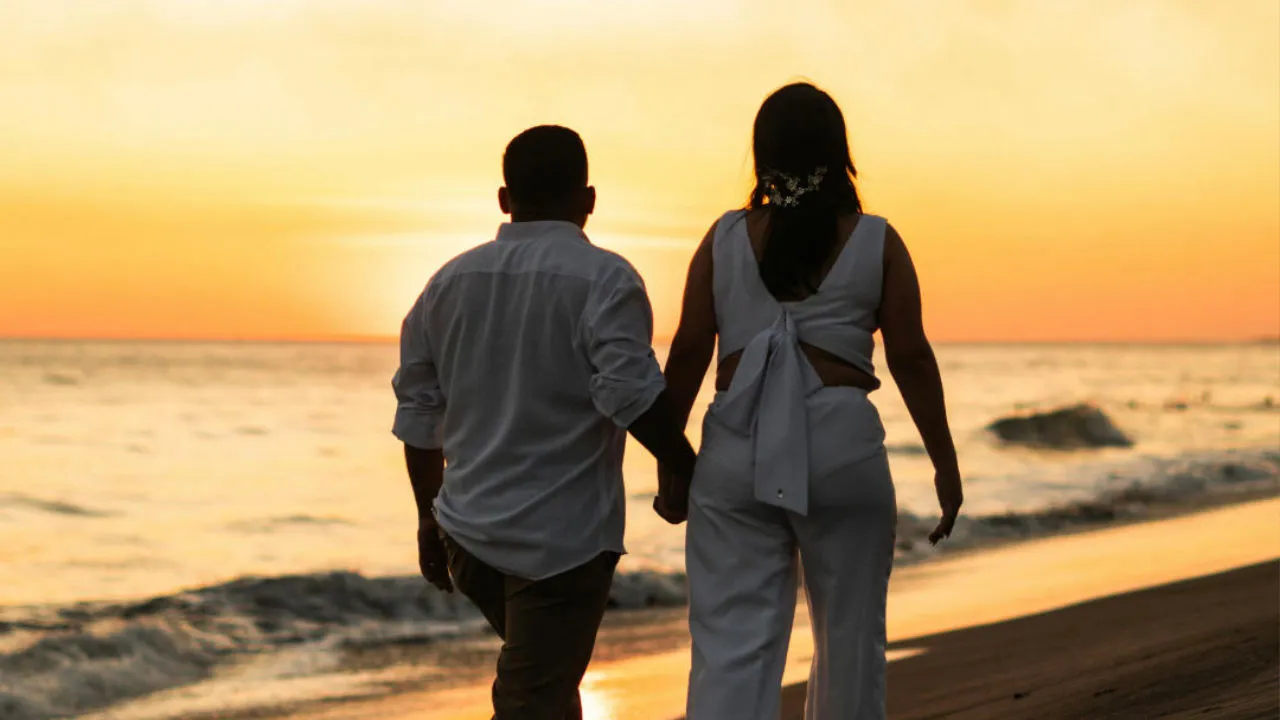 Couple holding hands walking on the beach at sunset