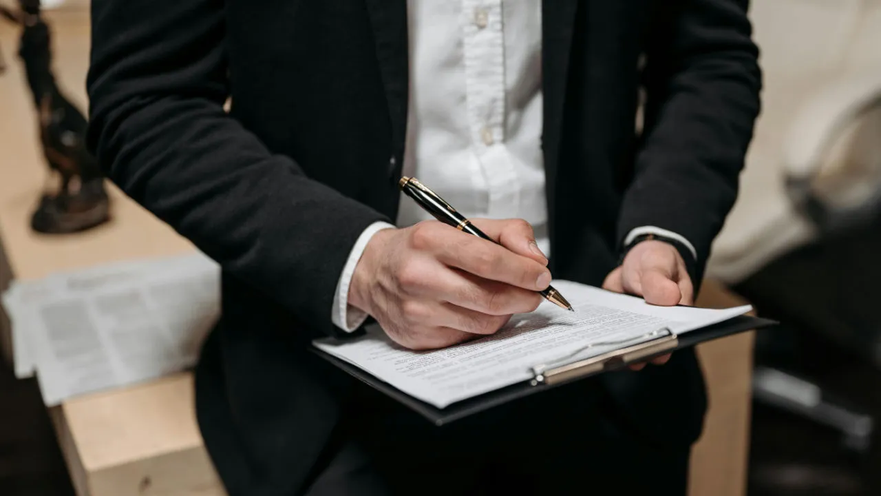 A professional in a business suit signing a document on a clipboard, representing a U.S. employer completing the hiring process for a TN visa professional.