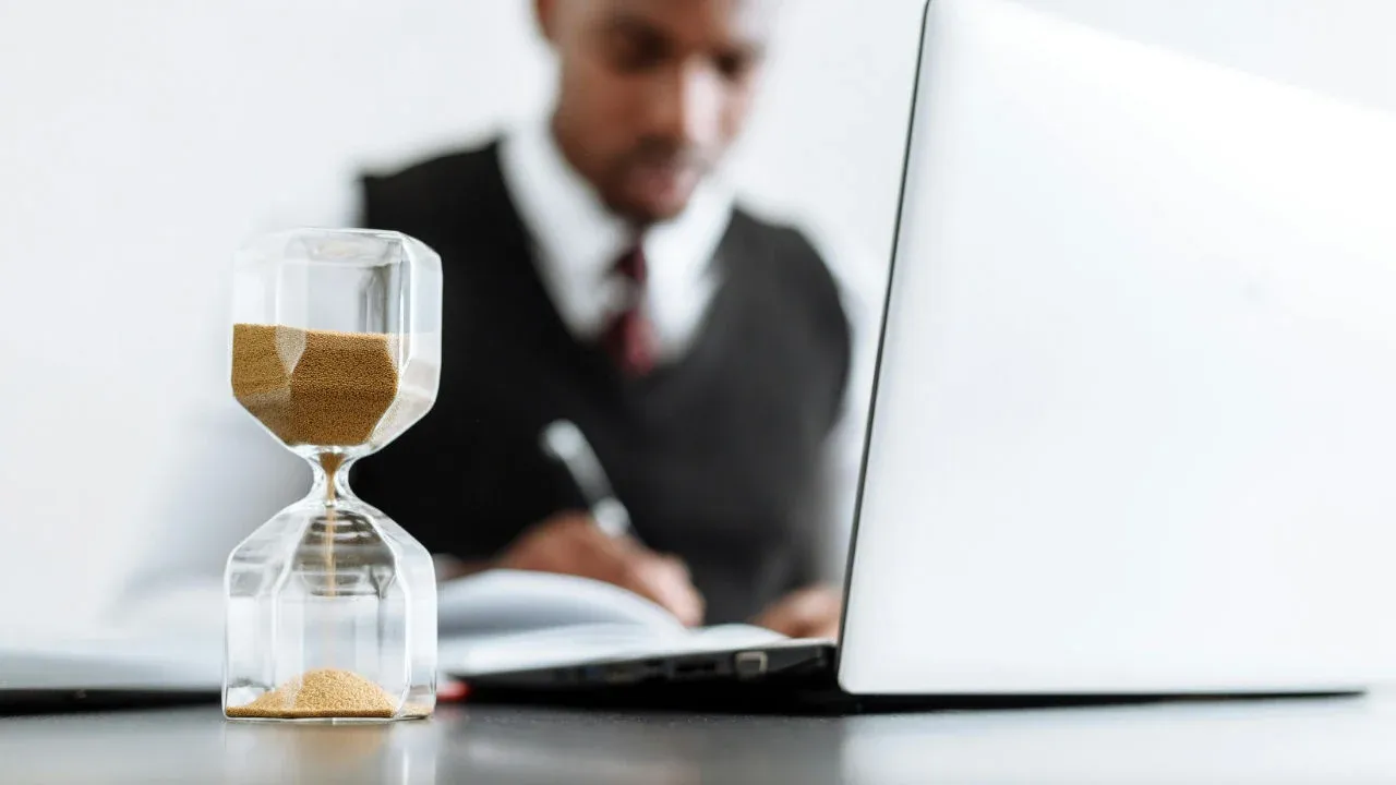 An hourglass on a desk in front of an E-2 investor, symbolizing the indefinite time limit for the E-2 visa.