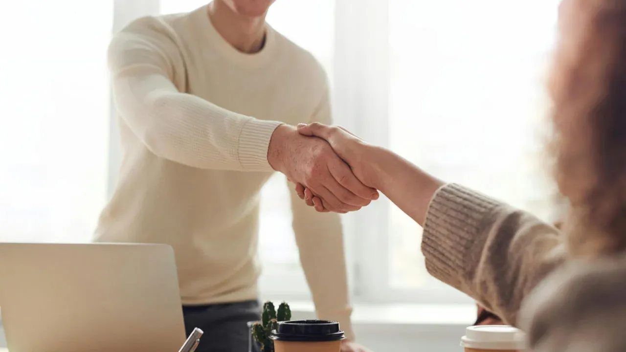 A business owner shaking hands with a new hire, representing the future hiring goals of an E-2 visa business plan.