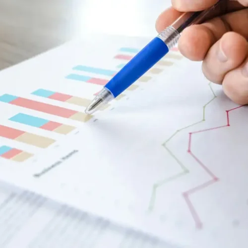 A hand holding a pen, pointing to financial charts on a business document, representing the E-2 visa business plan process.