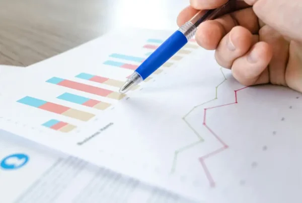 A hand holding a pen, pointing to financial charts on a business document, representing the E-2 visa business plan process.
