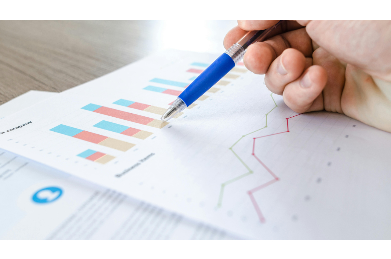A hand holding a pen, pointing to financial charts on a business document, representing the E-2 visa business plan process.