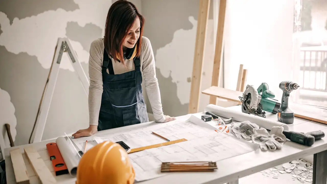 Female contractor examining architectural plans in a workshop, symbolizing the launch of a new business after a successful E-2 visa application.