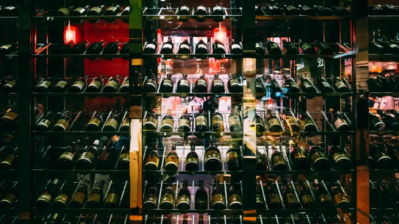 Floor-to-ceiling glass and metal shelves filled with hundreds of wine bottles in a modern liquor store.